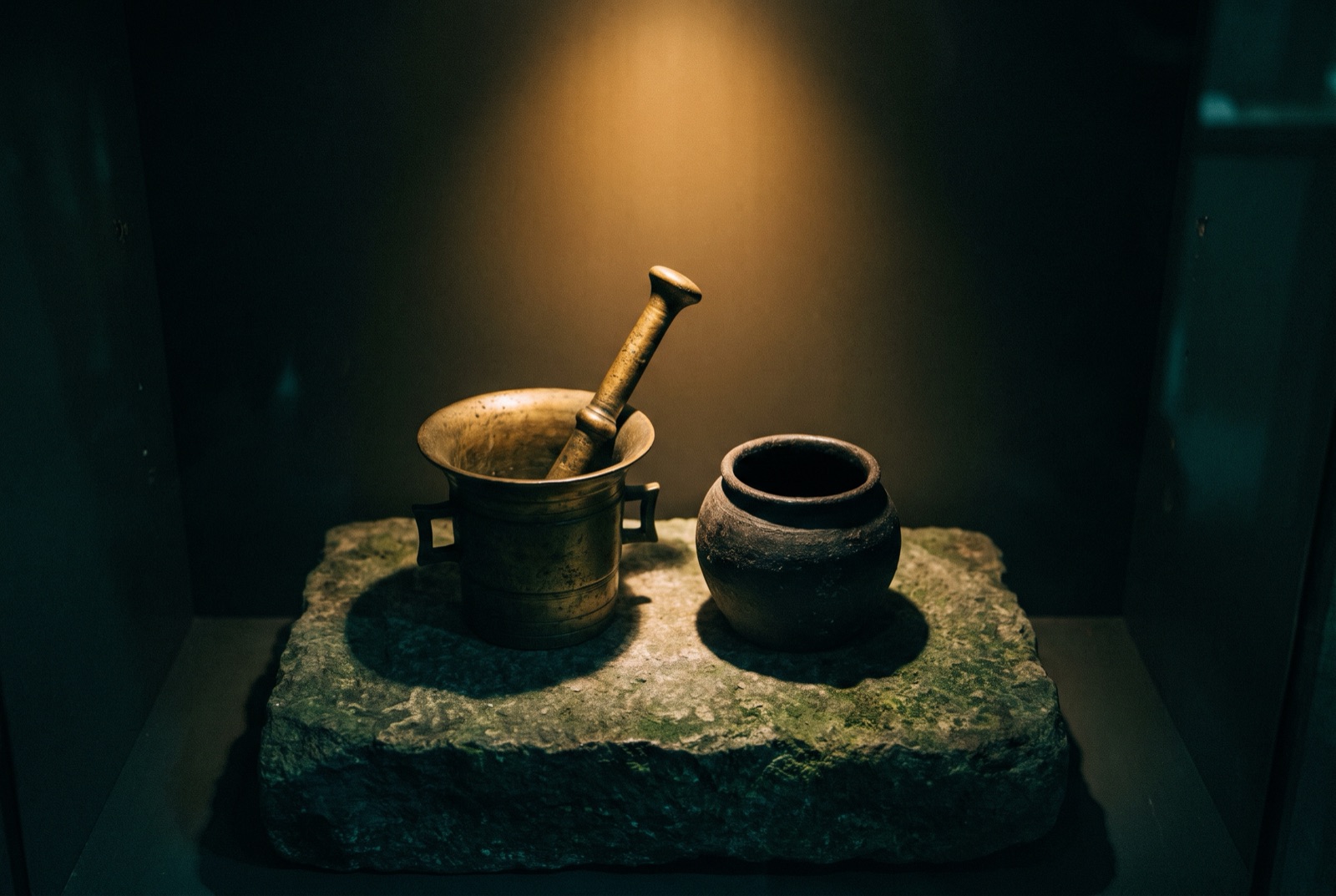 An ancient mortar and pestle beside an apothecary jar, its contents lost in shadow